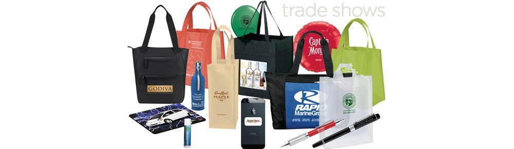 An assortment of custom-branded trade show giveaways: tote bags, a wine carrier, mouse pad, lip balm, frisbee, phone case, plastic bags, and pens.